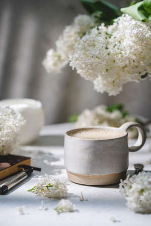 Spring composition with cup of coffee and white lilac beautiful bouquet. Concept of spring and comfortの写真素材