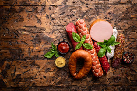 Set of different types of sausages, salami and smoked meat with basil and spices on wooden background. Top view.の写真素材
