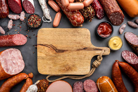 Set of different types of sausages, salami and smoked meat with basil and spices on a black...