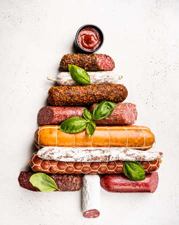 Christmas tree from different types of sausages, salami and smoked meat with basil and spices on white background. Top view.の写真素材