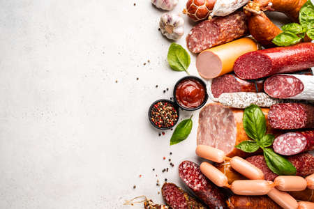 Set of different types of sausages, salami and smoked meat with basil and spices on white background. Top view.の写真素材