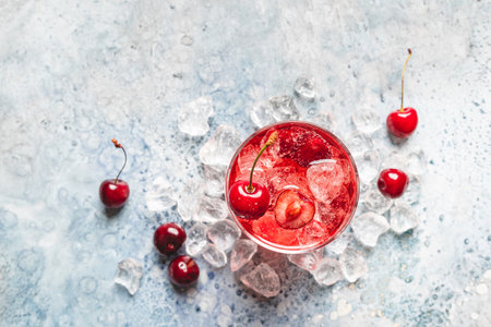 Cold sweet cherries lemonade with fresh sweet cherry and ice on white blue background, top view