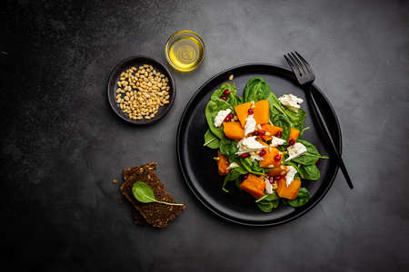 Salad with roasted pumpkin, cheese, spinach, Pine nuts and seasonings on dark background, top viewの写真素材