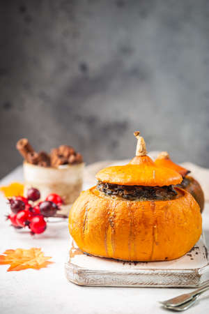 Tasty autumn stuffed pumpkin with fresh mushrooms, spinach and vegetables ready on rustic white tableの写真素材