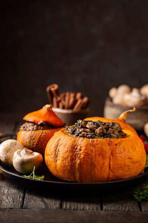 Tasty autumn stuffed pumpkin with fresh mushrooms, spinach and vegetables ready on rustic dark wooden tableの写真素材