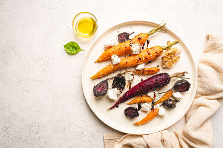 Roasted young whole colorful carrot with herbs and cheese served on plate over white background. Top viewの写真素材