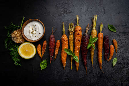 Roasted young whole colorful carrot with herbs over black background. Top viewの写真素材