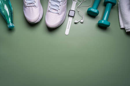Flat lay sport with shoes, bottle of water, dumbbells, watch, and earphones on green background....
