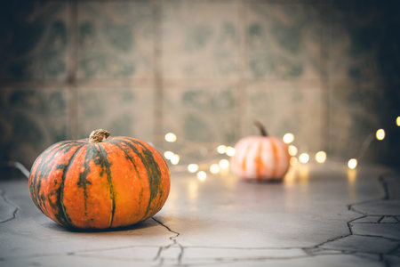 Thanksgiving or Halloween autumn decorations with mini green and orange pumpkins against a tile background and lights.の写真素材