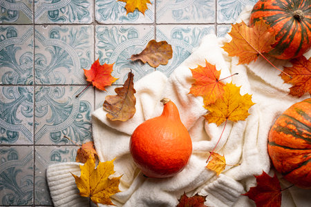 Cozy autumn flat lay with pumpkins, knitted woolen sweater and autumn leaves candle on tile background. Autumn home decor. Cozy fall mood. Thanksgiving. Halloween.の写真素材