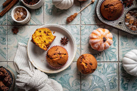 Homemade autumn pumpkin muffins with cinnamon and chocolate on tile background, top viewの写真素材