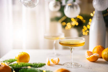 Two glasses of champagne and tangerines on a table against blurred christmas background with christmas lights. New year celebration partyの写真素材
