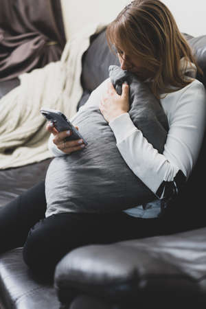 Unhappy lonely depressed woman at home, she is sitting on the couch and hiding her face on a pillow, depression conceptの写真素材