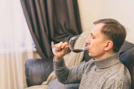 Relaxed serene rich lonely middle aged single man drinking red wine relaxing on sofa at home, enjoying resting sitting on couch holding glass tasting and reflecting.の写真素材