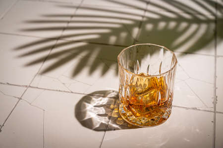 Whiskey with ice in glasses, white background with hard light, shadows and sun glare, copy spaceの写真素材