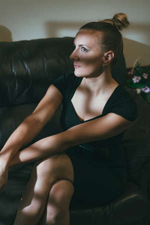 Portrait of gorgeous elegant sensual woman wearing black dress seating on the couch with bright shadowsの写真素材