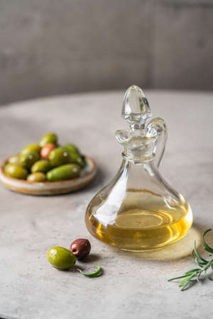 Olive oil in a glass bottle containers and harvest olives with herbs on gray background.の写真素材
