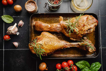 baked fried turkey thighs, rubbed with spices and salt on a baking sheet with garlic and rosemary on...