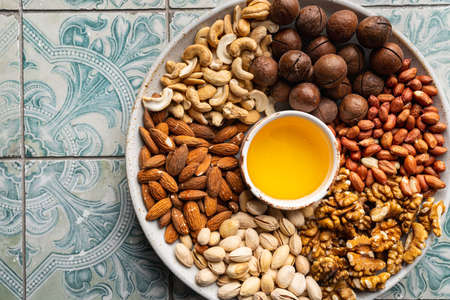 Assortment of nuts in a bowl with honey on blue tile background top view with copy space. Healthy snack food.の写真素材