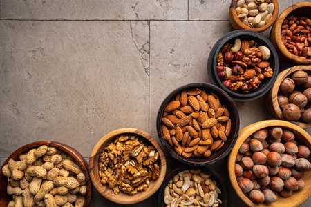 Assortment of nuts in bowls on stone background top view with copy space. Healthy snack food.の写真素材