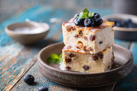 Baked homemade cottage cheese casserole or pudding with raisins serving with blueberry and sour cream on blue background. Close-up.の写真素材