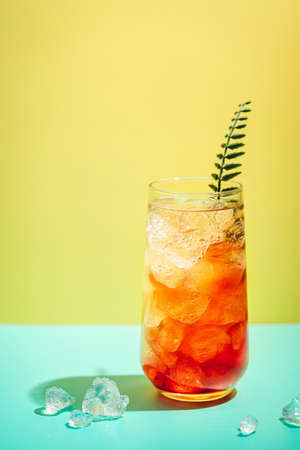 Glass of delicious summer tropical tequila sunrise cocktail with ice, isolated on yellow background