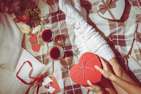 Valentine Day celebration flat lay with present in heart-shaped box and womans legs in white socks on bed or floor background, top viewの写真素材