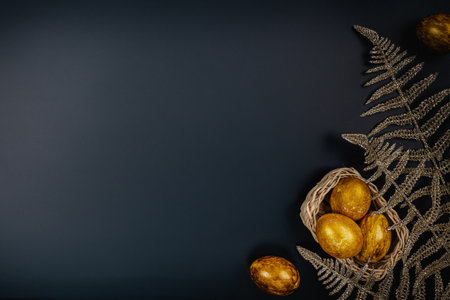 Golden and silver Easter eggs in a basket and gold branches on black table background, top view