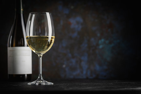 A dark, elegant still life of white wine in a glass with wooden background. Perfect for wine-themed compositionsの写真素材