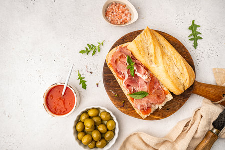 Baguette sandwich with prosciutto or jamon ham serrano paleta, tomato sauce and basil on white background, top viewの写真素材