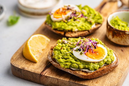 Toast with avocado, feta cheese, eggs, herbs and seeds with lemon slices on white background. Healthy eating and wholesome Breakfastの写真素材