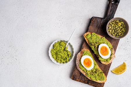 Toast with fresh avocado, eggs, herbs and seeds with lemon slices on white background. Healthy eating and wholesome Breakfast, top viewの写真素材