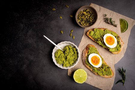 Toast with fresh avocado, eggs, herbs and seeds with lemon slices on dark background. Healthy eating and wholesome Breakfast, top viewの写真素材