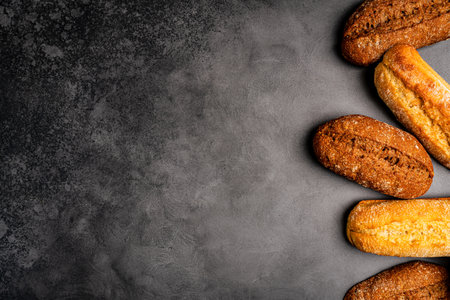 Bakery various kinds of breadstuff. Bread classic and mini baguette and buns captured from above (top view, flat lay). Black background, free copy space.の写真素材