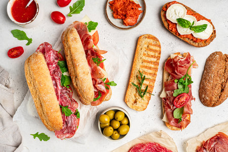 Assorted delicious baguette sandwiches filled with thinly sliced ham or salami and fresh green lettuce or arugula for breakfast arranged on white background, top view with copy spaceの写真素材