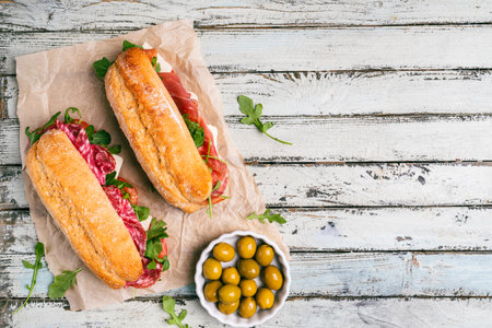 Assorted delicious baguette sandwiches filled with thinly sliced ham or salami and fresh green lettuce or arugula for breakfast arranged on white background, top view with copy spaceの写真素材