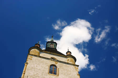 Old church tower in front of a cloud and a blue skyの写真素材