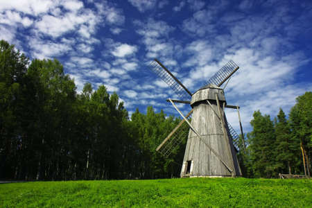 Old rural windmill on a meadow, surrounded by forest. High-contrast cloudscape.の写真素材
