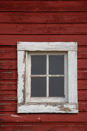 Square window with a white frame on an old red barn.の写真素材