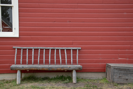 Timber bench and box against a red sided house with a white framed window paneの写真素材