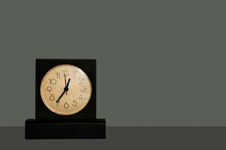 Black table clock with white dial standing on dark table isolated on dark backgroundの写真素材