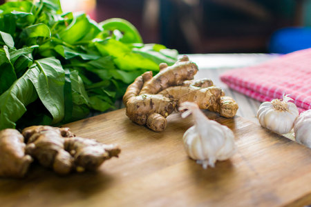 Whole raw fresh ginger place on a wooden chopping board surrounded by kitchen towel, whole garlic and herbs selective focus photography with shallow depth of fieldの写真素材