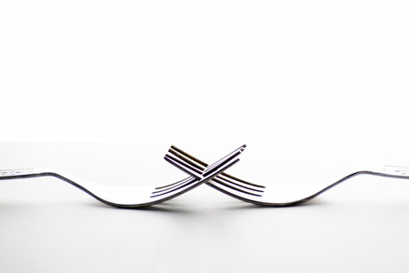 Engraved silverware fork set of two placed face to face crossing their teeth isolated on white...
