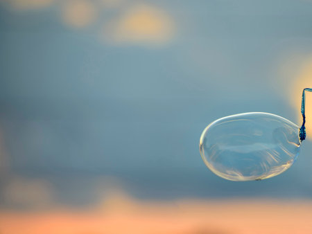 Huge crystal clear bubble is made by a soap bubble wand on blurred cloudy background