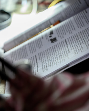 A close-up view of an open textbook lying on a desk, with softly blurred surroundings and natural ambient lighting, evoking themes of learning, education, and focus.の写真素材