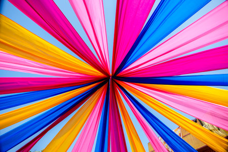 Brightly colored blue, yellow, and pink fabric strands form a decorative outdoor canopy, creating a festive and joyous atmosphere, ideal for events and celebrations in sunny surroundings.の写真素材