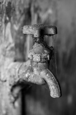 A black and white photograph of a vintage outdoor metal water faucet, showcasing its rustic texture and timeless design against a blurred background, emphasizing industrial decay and minimalist aesthetics.の写真素材