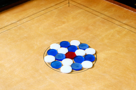 Carrom board with red, blue, and white coins neatly arranged in the center circle, highlighting an...