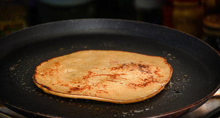 A close-up of a golden-brown pancake sizzling on a black nonstick pan, highlighting breakfast...