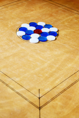 Carrom board with red, blue, and white coins neatly arranged in the center circle, highlighting an...
